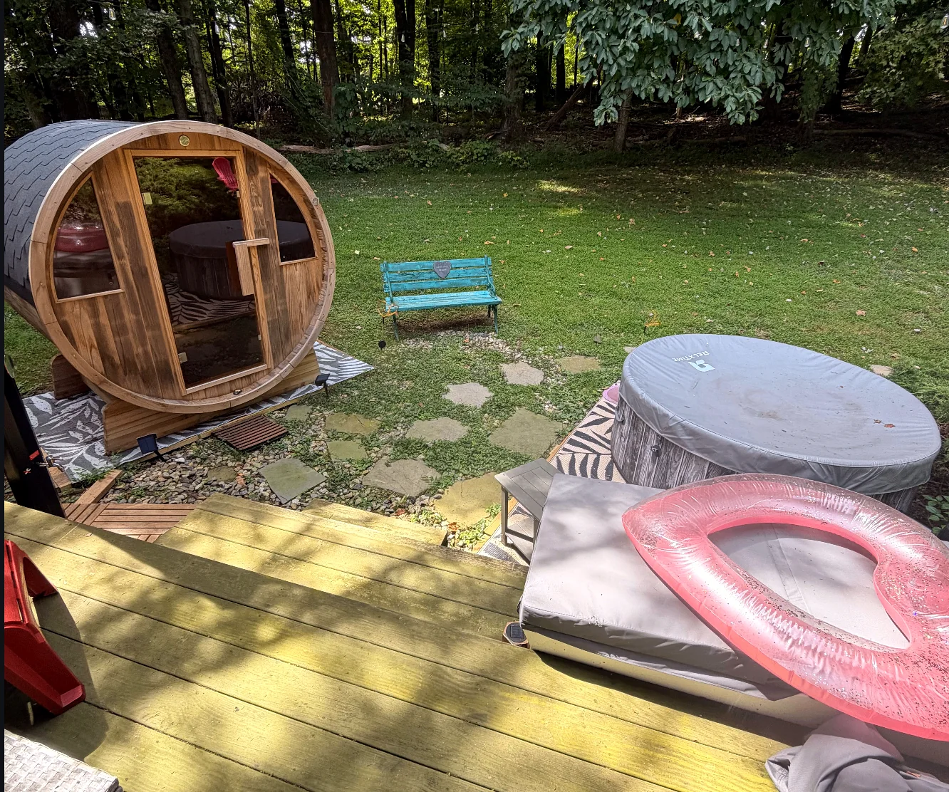 Barrel sauna and round hot tub on a wooded patio