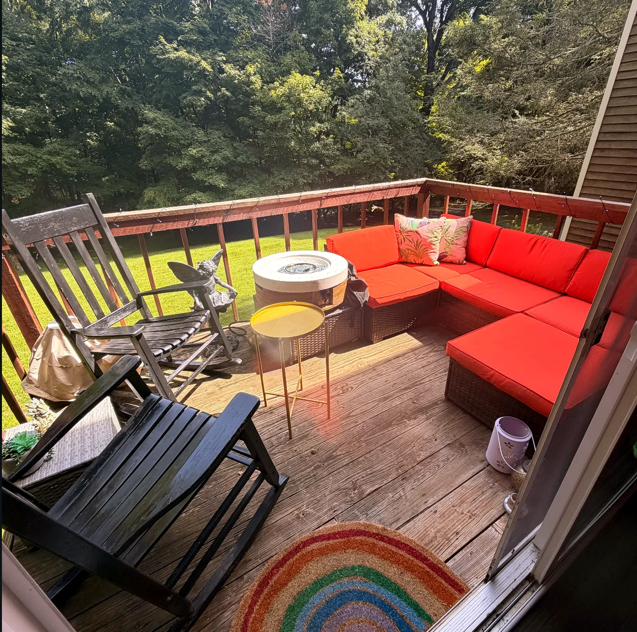 Upper deck with a red sectional and fire table overlooking the woods