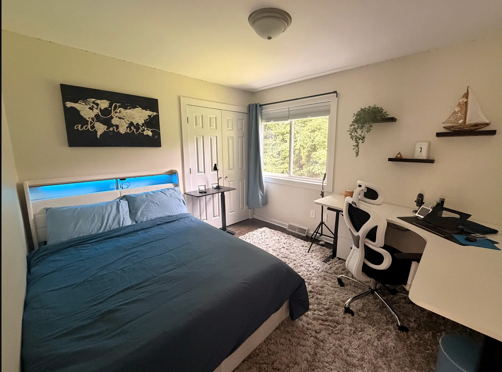 Blue bedroom with a bed, desk, and windows